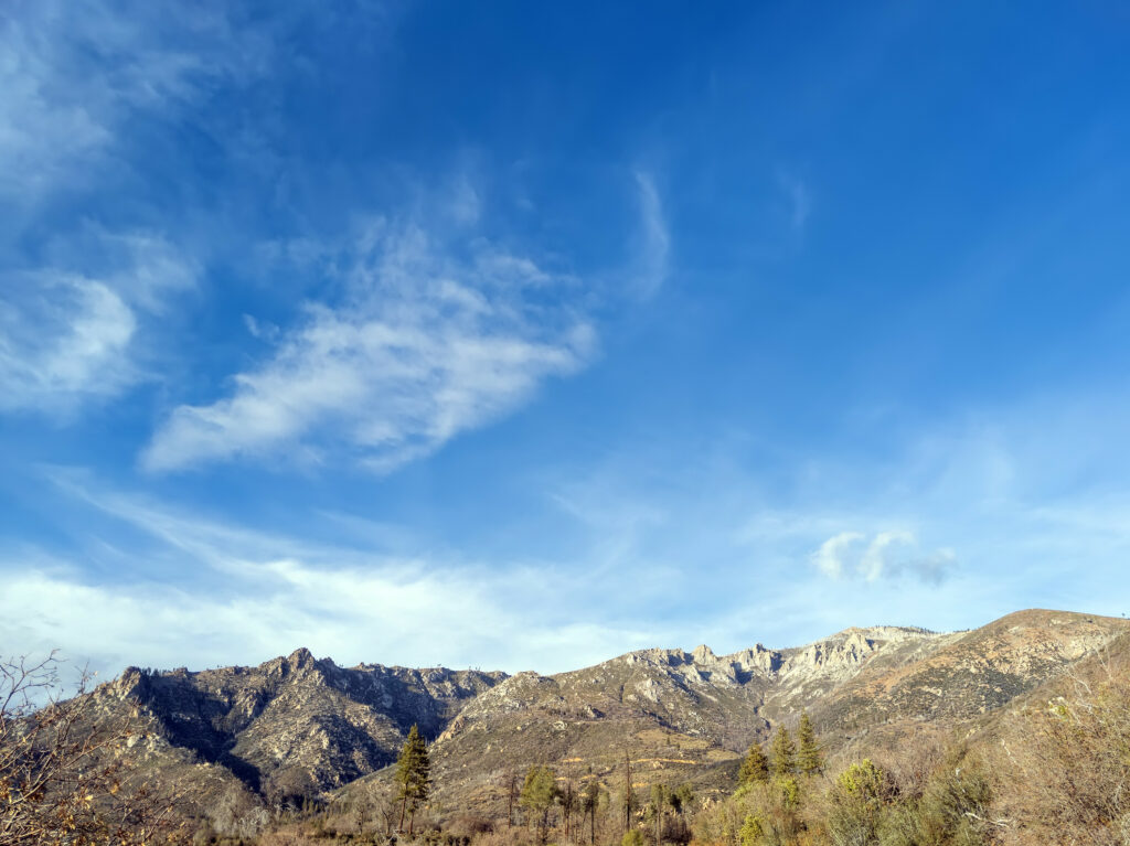 Rugged mountain range with rocky peaks under vibrant blue sky and wispy clouds wallpaper background