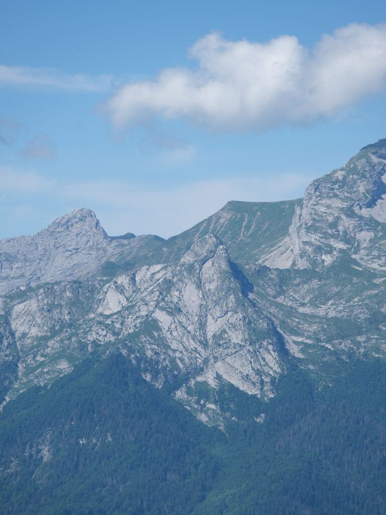 Rugged mountain slopes with dense trees under vibrant blue sky and scattered clouds wallpaper
