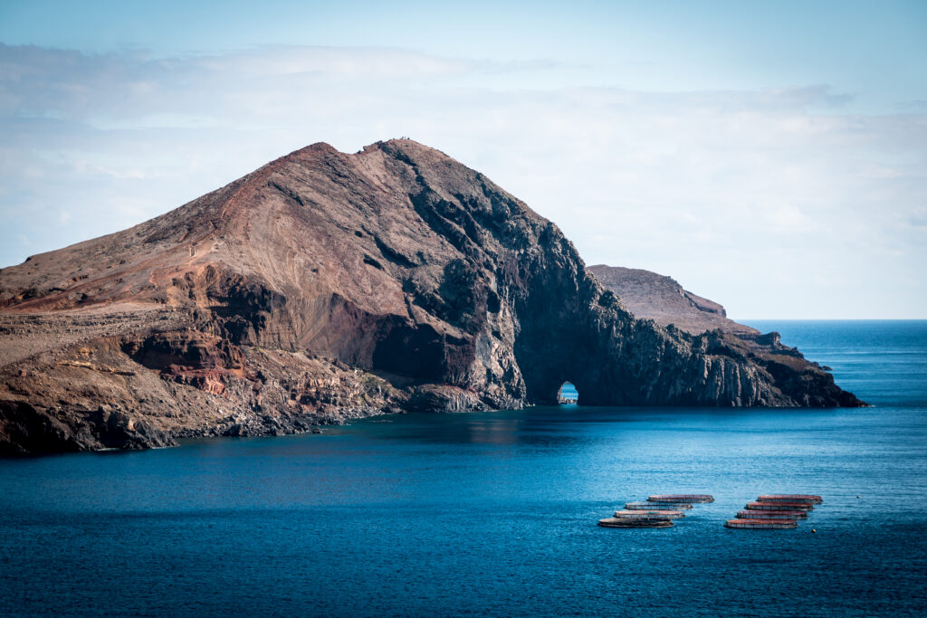 Majestic rugged rock island with cliffs rising from deep blue sea and boats nearby coastal scene Wallpaper