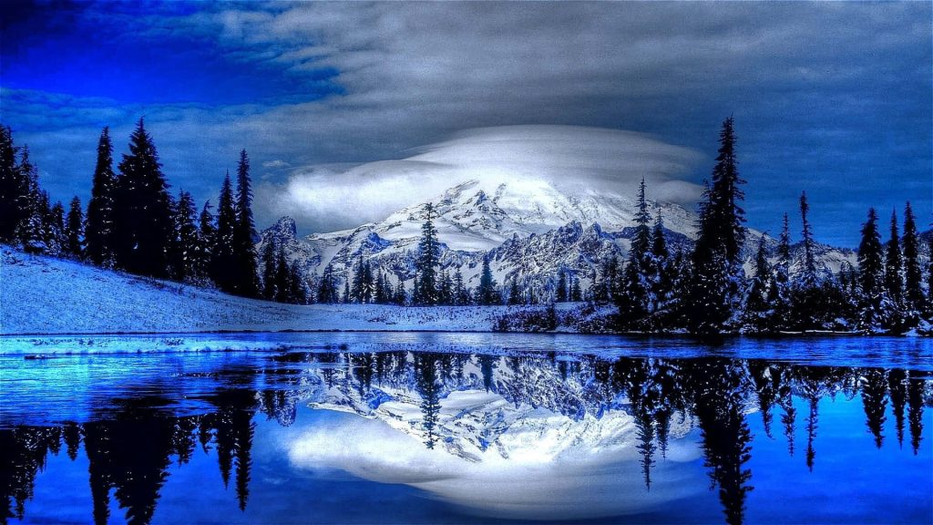 Snow-capped Mount Rainier reflected in calm lake with evergreen trees and blue sky background Wallpaper