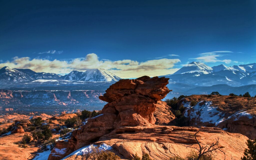 Striking canyon landscape with rugged stones snow patches and snow-capped mountains under blue sky Wallpaper