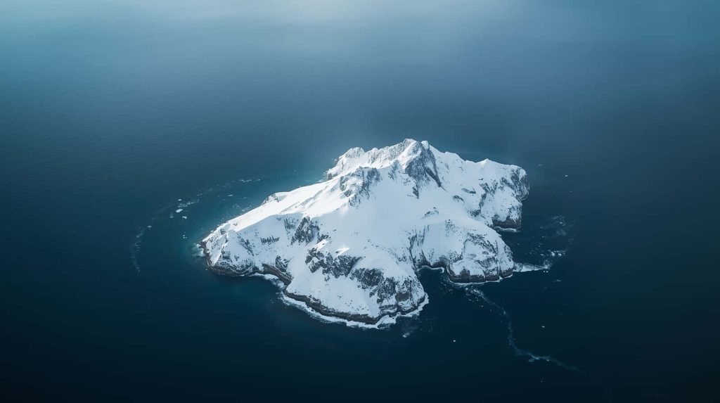 Aerial view of sharp snow-capped mountain island surrounded by serene deep blue ocean waters Wallpaper