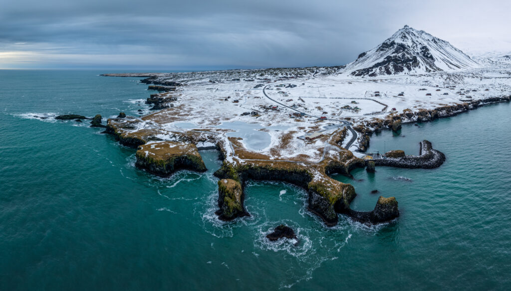 Snow-capped mountain island with turquoise sea rugged cliffs and swirling clouds wallpaper background