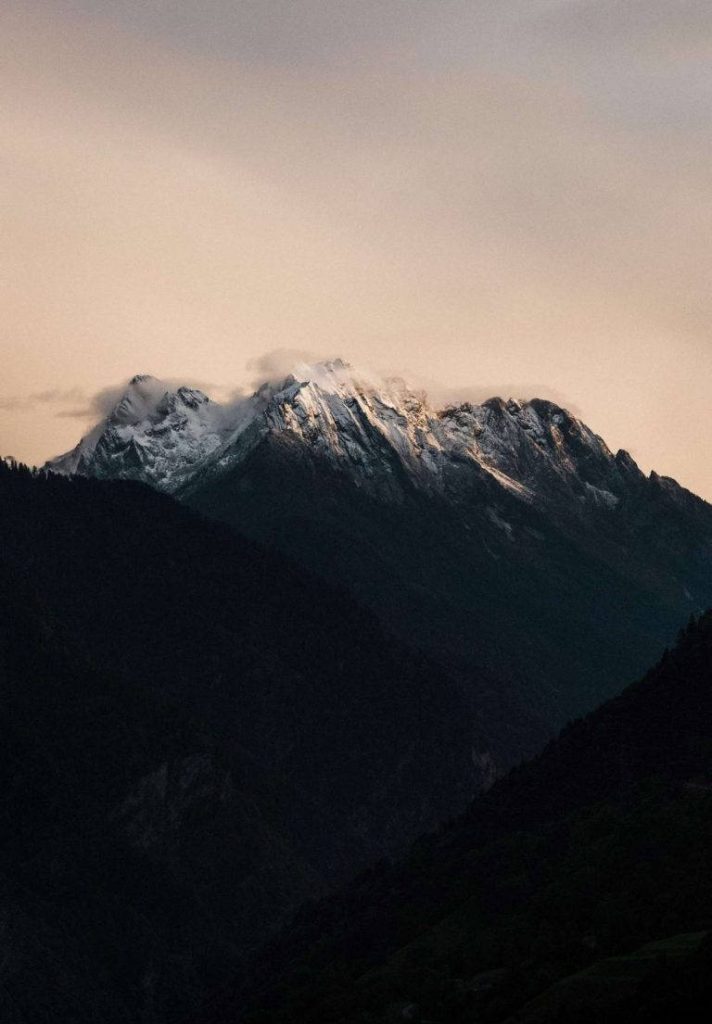 Majestic snow-capped mountain at sunset with pastel sky and dark shadowed foreground slopes Wallpaper