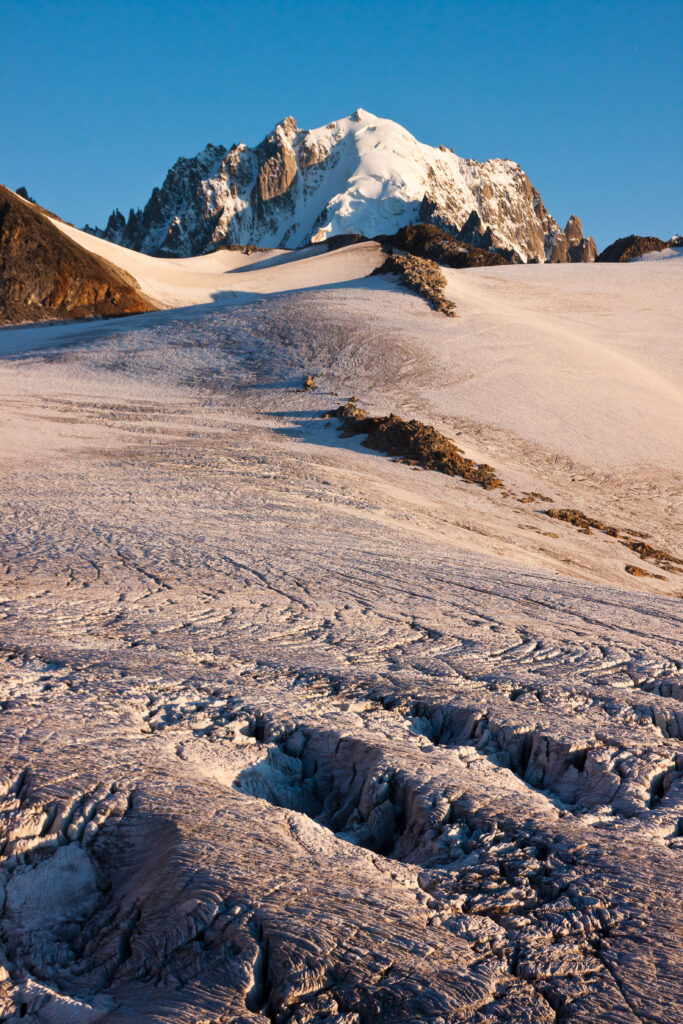 Snow-capped mountain with rugged rocks and textured snow under clear blue winter alpine sky wallpaper