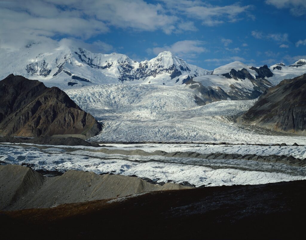Snow-capped mountains with rugged stones and sandy terrain under a vibrant blue sky wallpaper