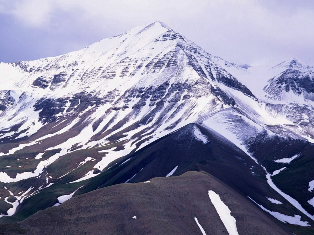 Snow-capped majestic mountains with rugged terrain and natural patterns in a serene winter landscape Wallpaper