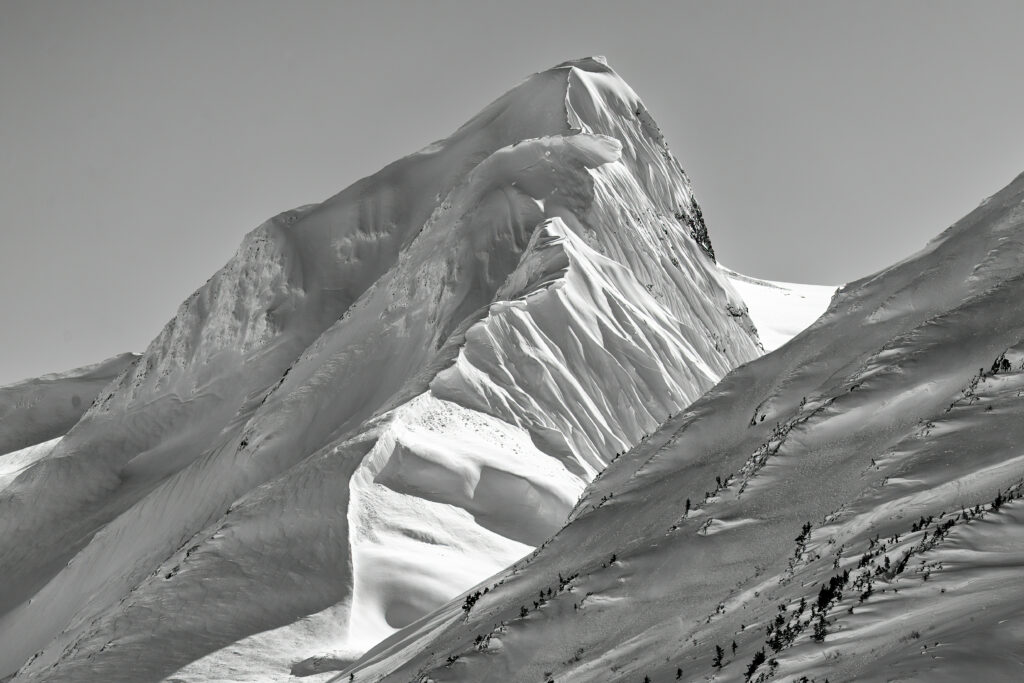 Snow-covered mountain slope with sharp ridges and textured relief under clear blue skies wallpaper
