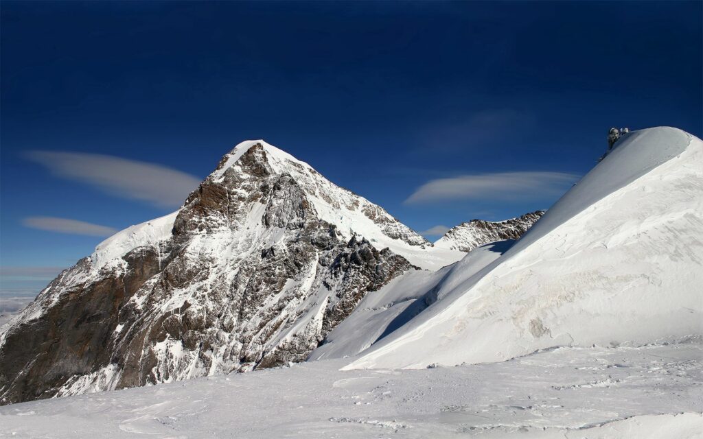 Majestic snow-covered mountain with geometric snow curves under deep blue winter sky wallpaper