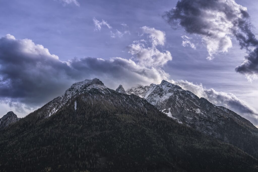 Majestic snow-capped mountain range under textured cloudy sky with forested slopes serene wallpaper