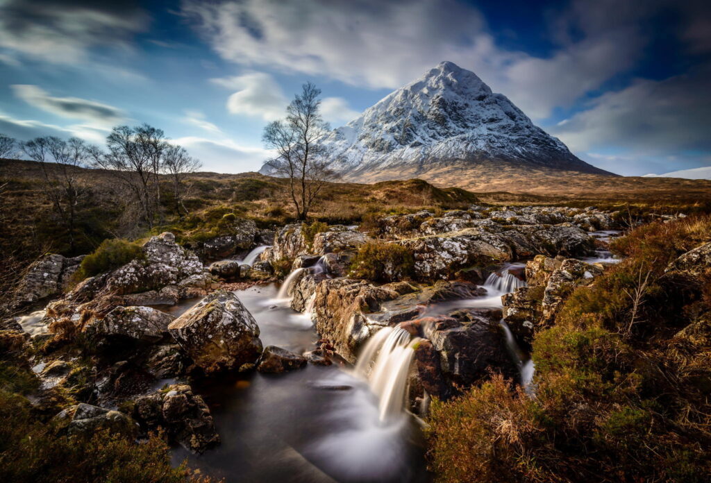 Snowcapped mountain over lush valley with winding river grassy fields and dramatic skies wallpaper