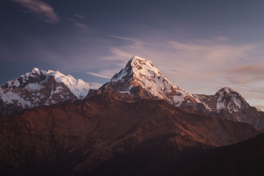 Sunset-lit snow-capped mountain range with rugged rocky peaks in a serene natural landscape wallpaper
