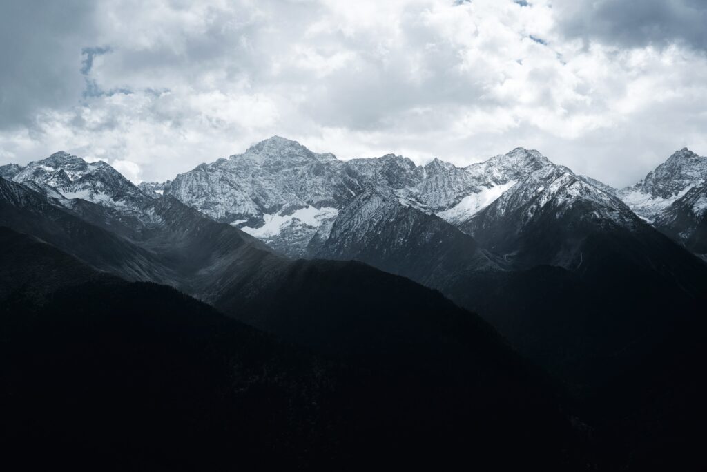 Dramatic snow-dusted mountain range under cloudy sky with light and shadow contrast wallpaper