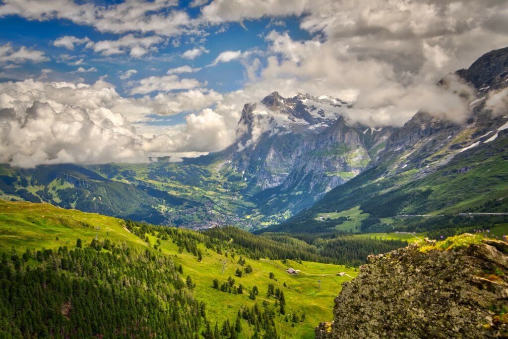 Snow-capped mountains over lush green valley with dense forest and dramatic cloudy blue sky wallpaper