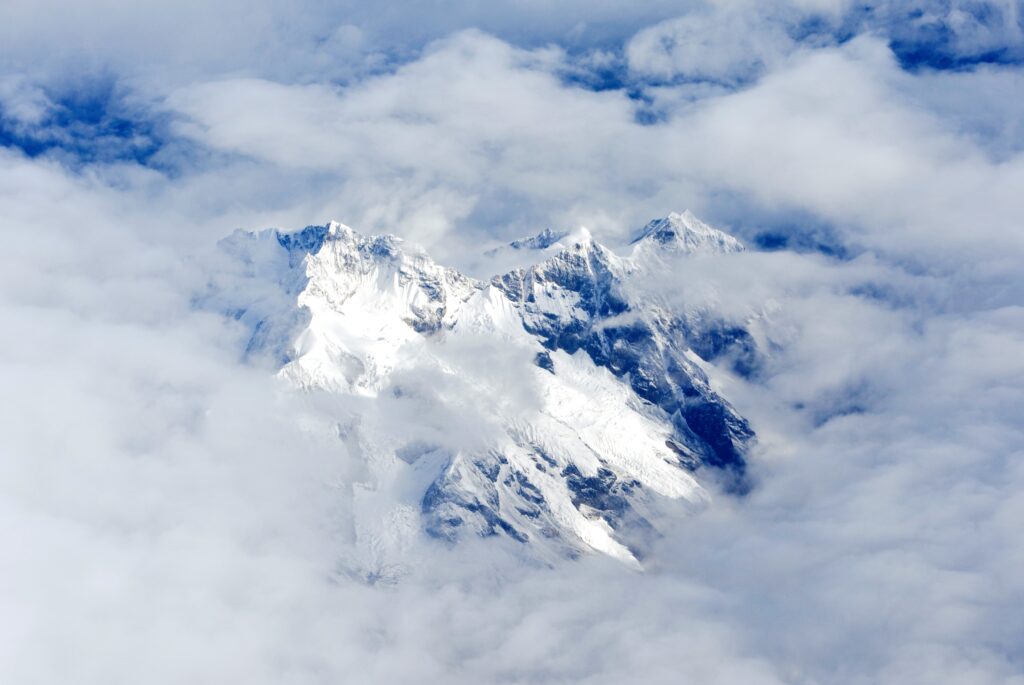 Snow-capped mountain peaks through soft clouds under bright sky serene high altitude landscape Wallpaper
