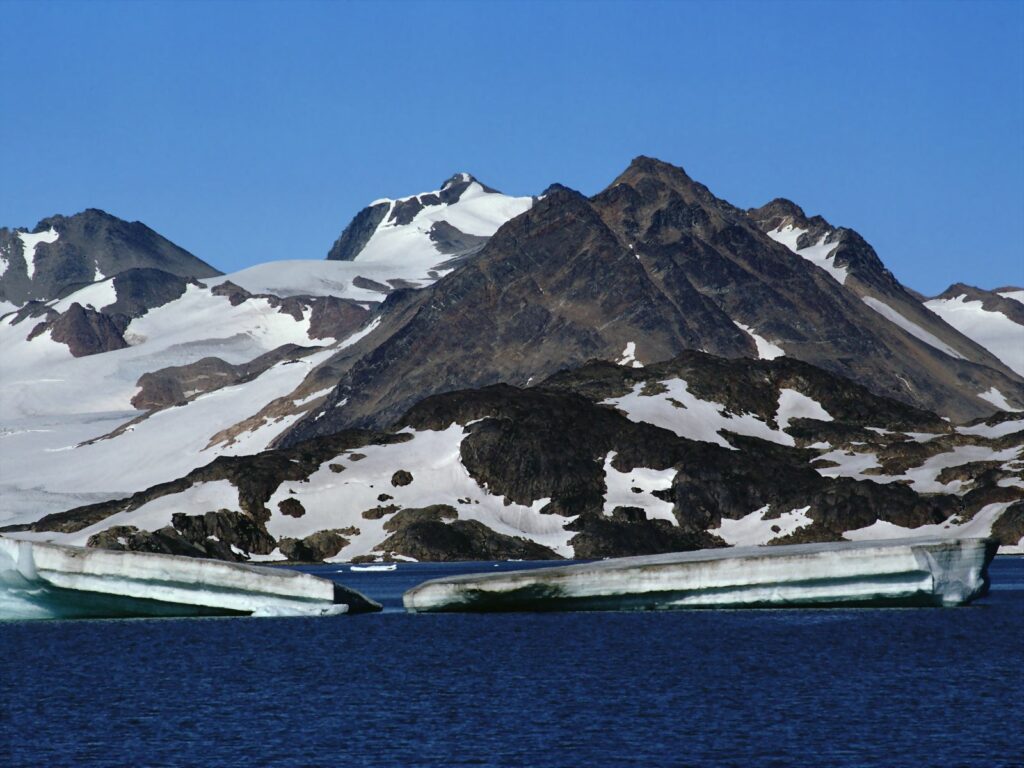Snow-capped mountains and glacier reflect in clear blue water under a vibrant blue sky wallpaper