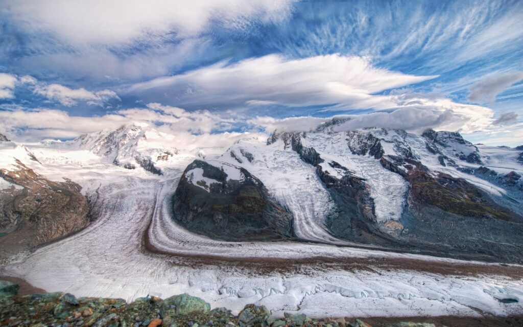 Snow-capped mountains with rugged glaciers and dramatic cloudy sky for wallpaper background