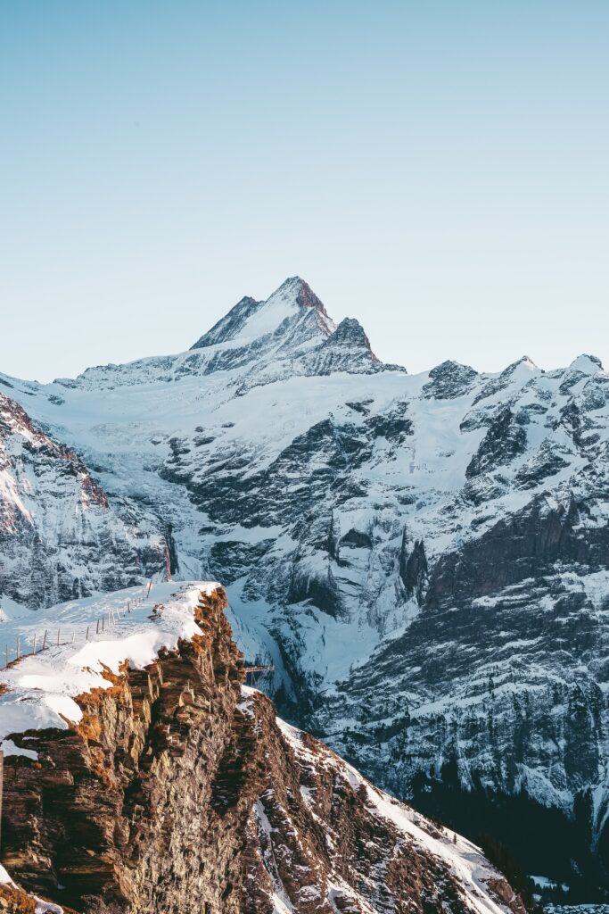 Snow-covered rugged mountain peaks under clear blue sky creating serene winter landscape wallpaper