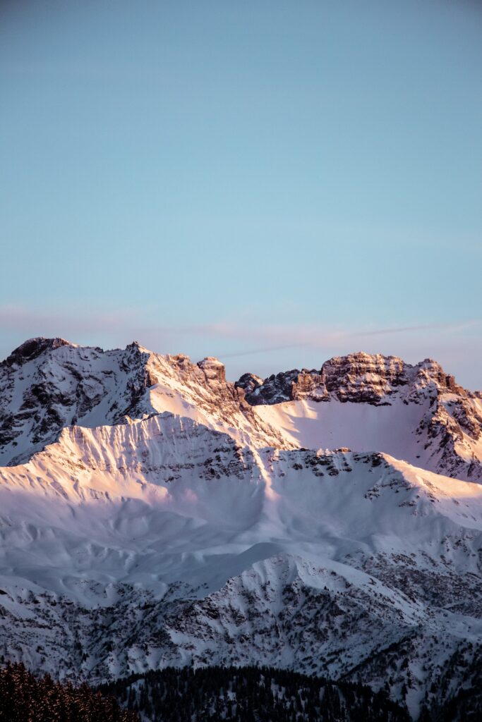 Snow-covered alpine mountains at sunset with rugged peaks and a serene sky wallpaper background