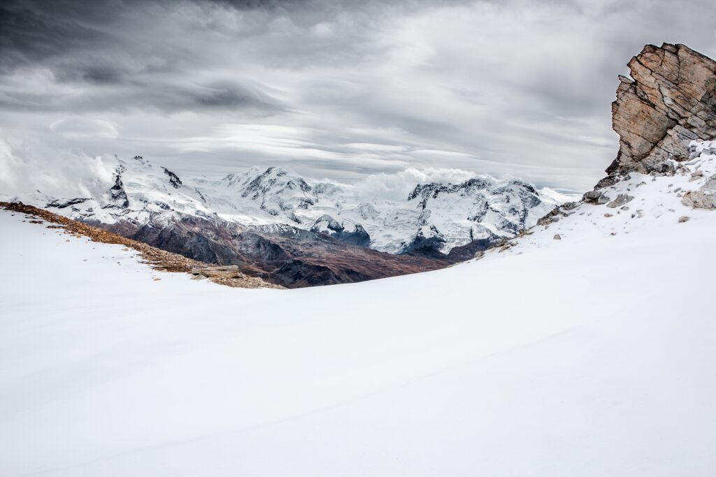 Snow-covered towering mountains with rugged rocks and swirling cloud sky pristine landscape wallpaper