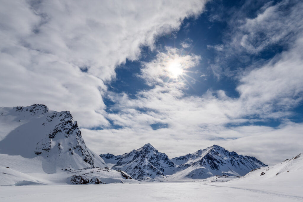 Snow-covered mountains under dramatic winter sky with sunlight breaking through clouds wallpaper