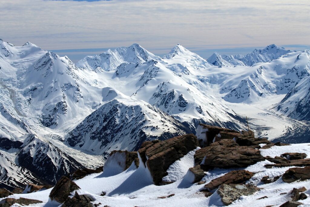 Snow-covered New Zealand mountains with rugged peaks and rocky foreground under soft sky Wallpaper