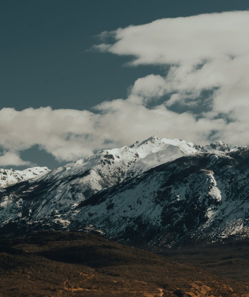 Snow-capped rugged mountains under dramatic cloudy sky serene wintry natural earthy wallpaper