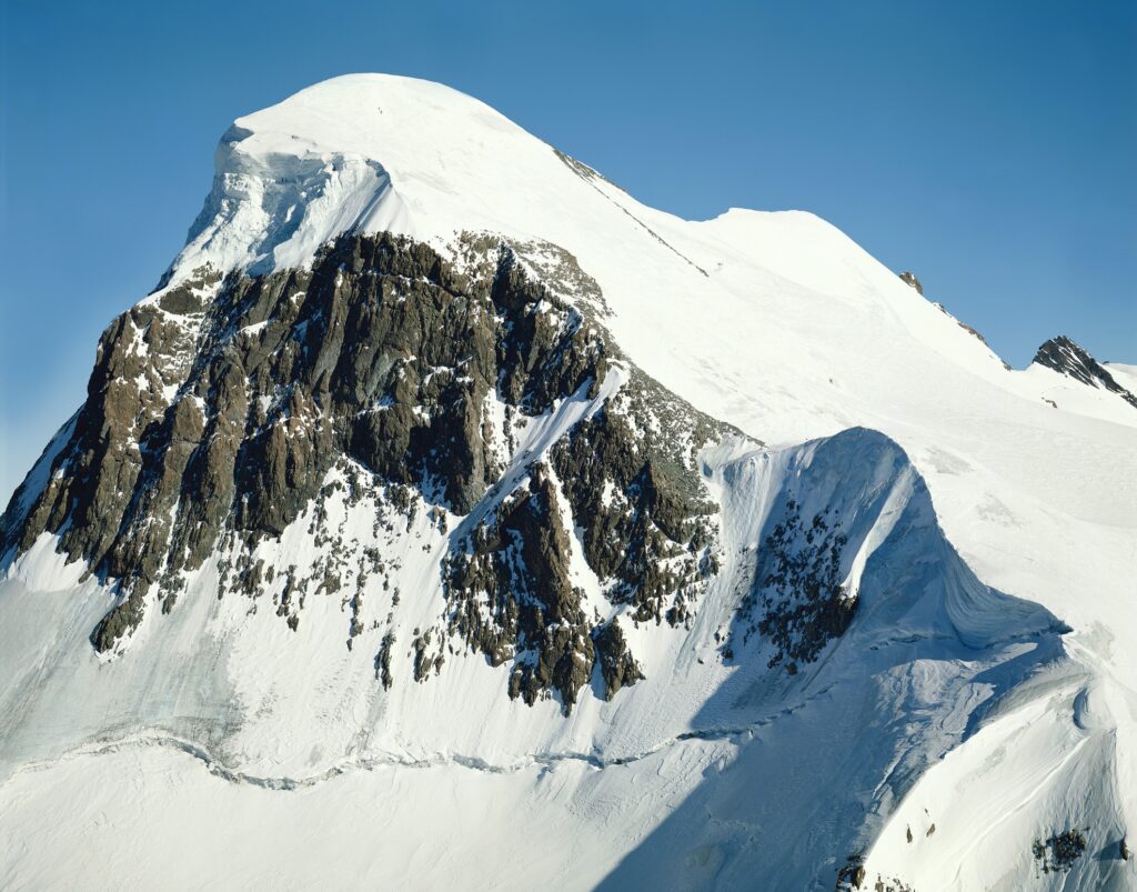 Towering snow-covered mountain peak with rugged rocks under a clear blue sky wallpaper background