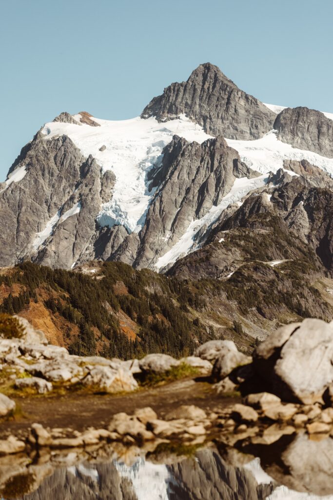 Majestic snow-capped mountain with rugged rocks and green trees under clear blue sky wallpaper