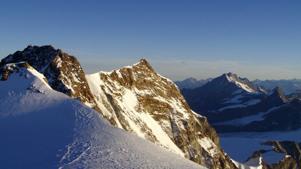 Snow-covered towering mountain peaks with rugged rocks under clear blue sky wallpaper background
