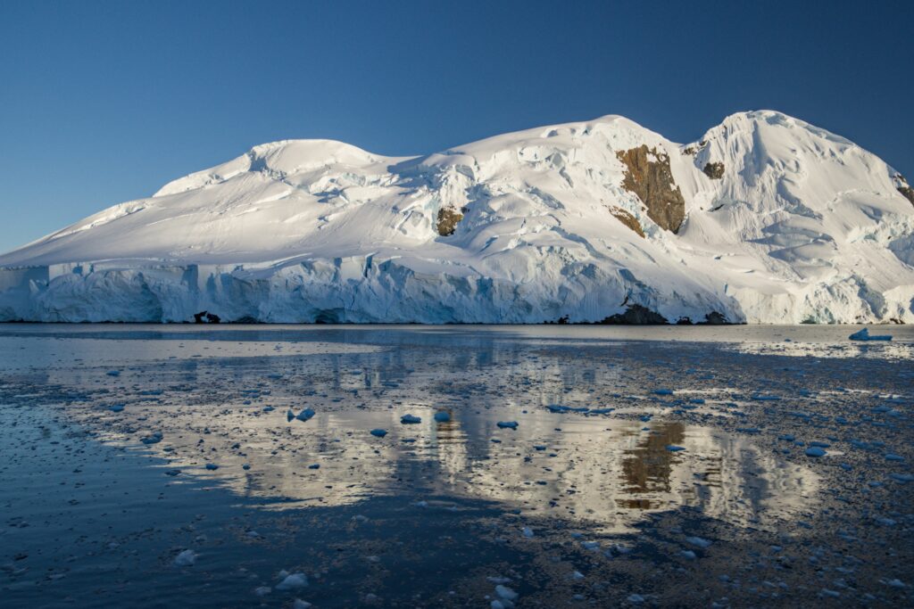 Snowy mountain with icebergs reflecting on calm sea under clear blue sky polar landscape wallpaper