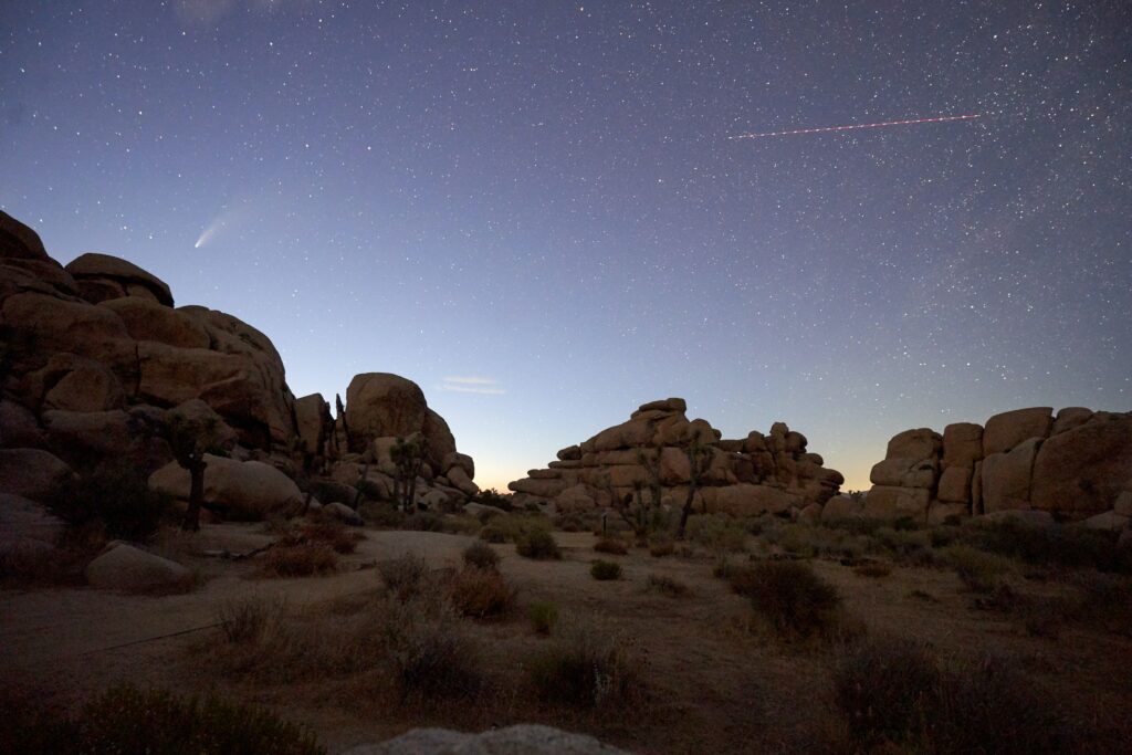 Tranquil night sky with starfall over massive rock formations in serene earthy and blue tones Wallpaper