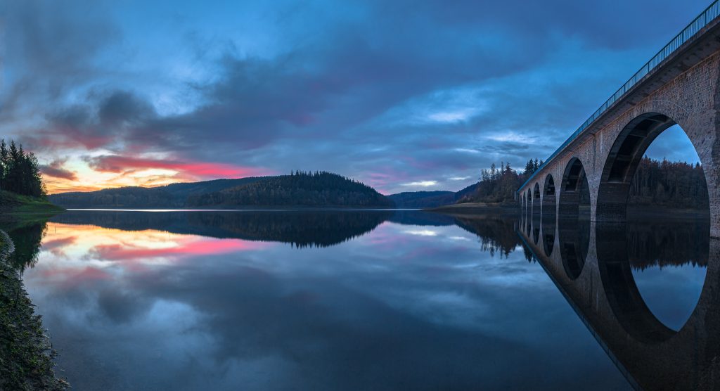 Majestic stone bridge arches reflected in calm water at twilight with soft blue and pink sky Wallpaper