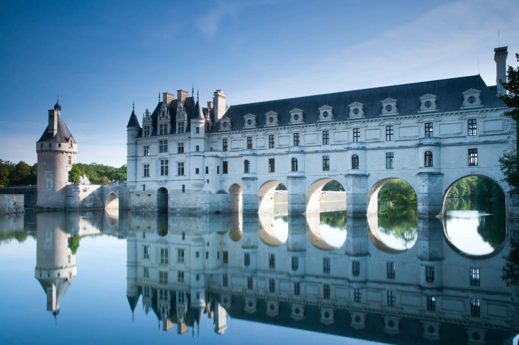 Majestic stone castle with elegant arches and towers reflected in calm river under stormy sky Wallpaper