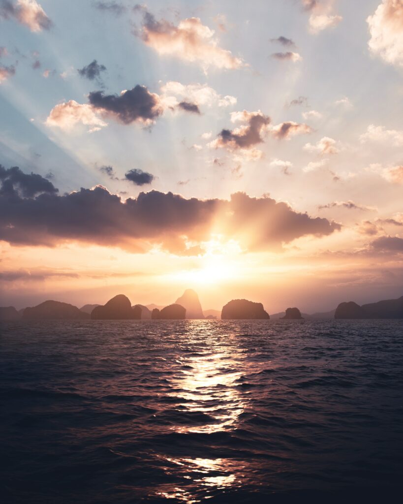 Golden sunset over calm sea with rocky silhouettes and warm glowing rays through clouds Wallpaper