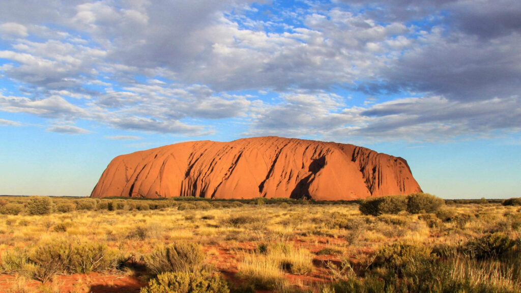 Uluru rock formation rising from golden desert under bright blue sky in Australian Outback wallpaper
