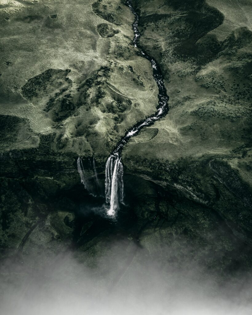Aerial view of majestic waterfall cascading through lush green landscape with mist and fog Wallpaper