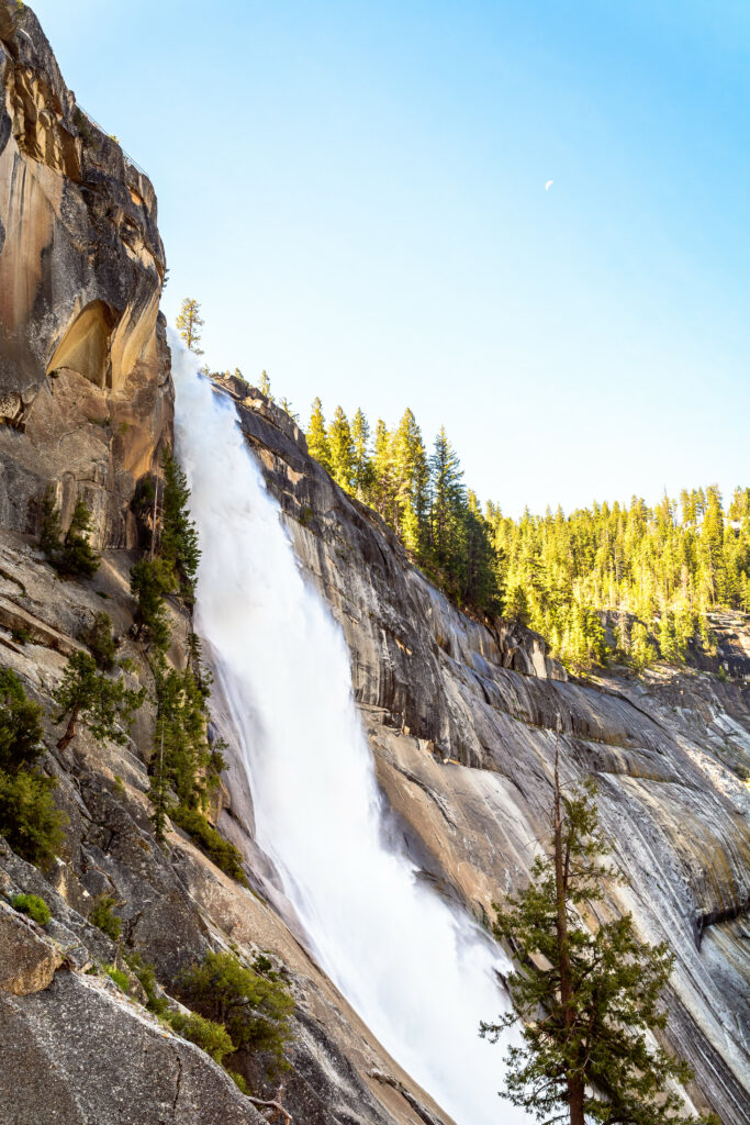 Stunning waterfall cascading down rugged rocks and cliffs surrounded by lush green forest sky Wallpaper