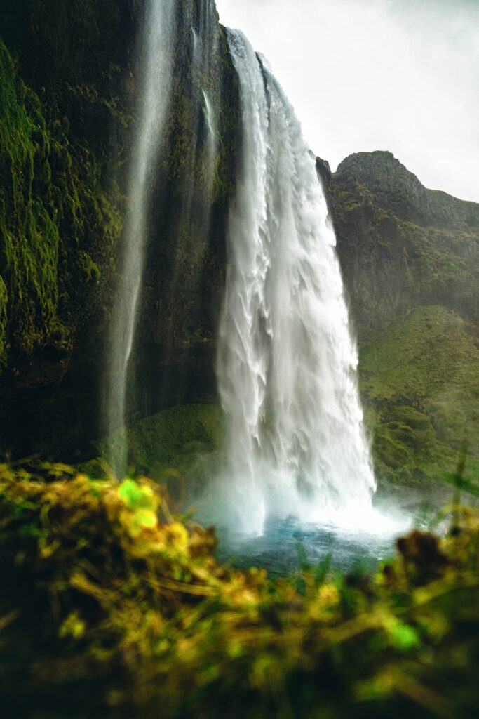 Majestic waterfall cascading over mossy cliff into a serene pool with vibrant natural colors Wallpaper