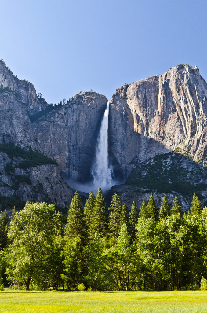 Majestic waterfall cascading over rugged rocks surrounded by lush green trees and sunlight Wallpaper