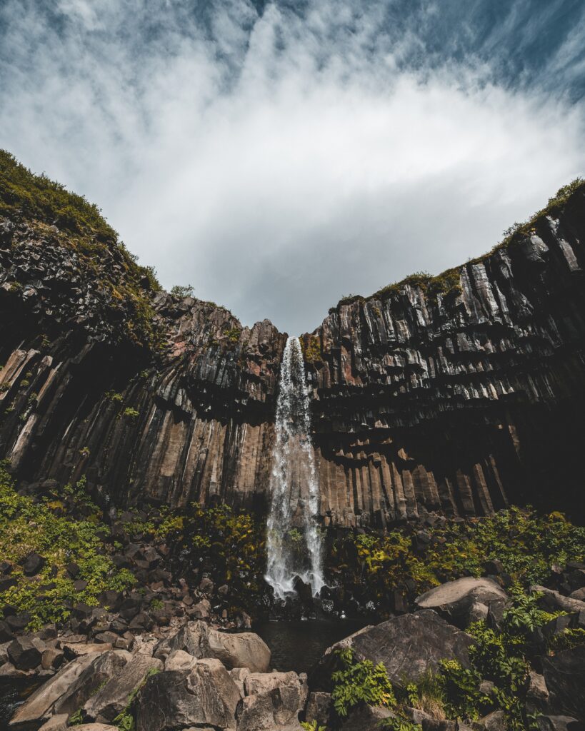 Waterfall cascading down dramatic stone cliffs with lush greenery and vertical rock formations Wallpaper