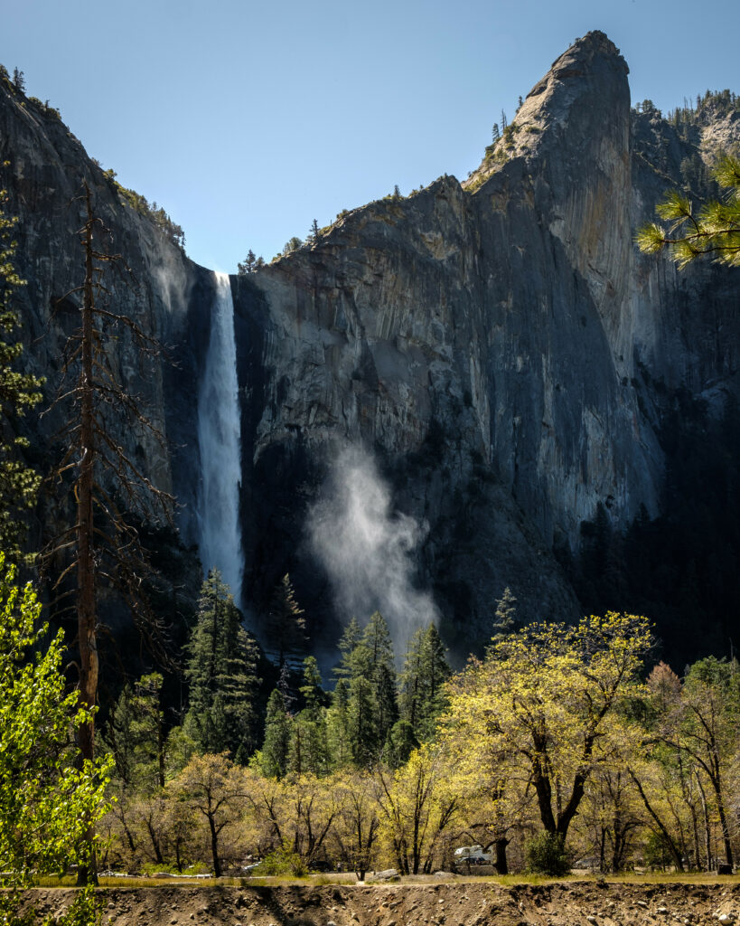 Majestic waterfall cascading down rocky cliffs surrounded by lush green trees in daylight Wallpaper