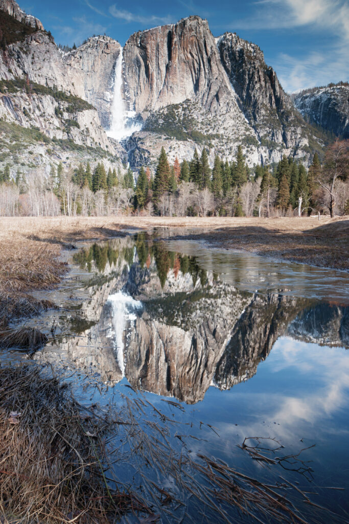 Majestic waterfall cascading rugged cliffs with lush pine trees and vibrant reflective water Wallpaper
