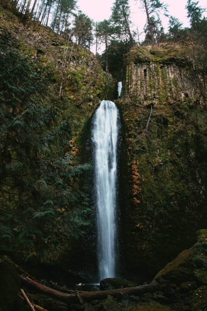 Majestic waterfall cascading down mossy cliff with lush greenery and clear stream below wallpaper