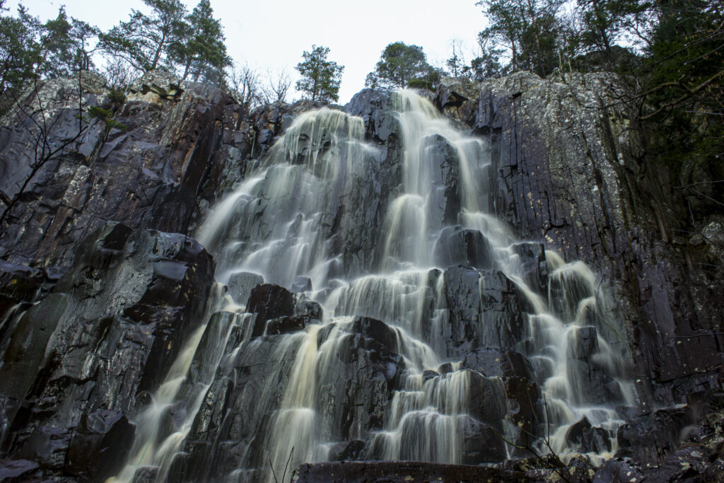 Waterfall cascading over rocks surrounded by cliffs and tall trees in serene wilderness wallpaper
