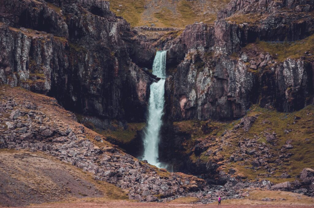 Majestic waterfall cascading over rugged rocks with towering earthy mountains in background wallpaper