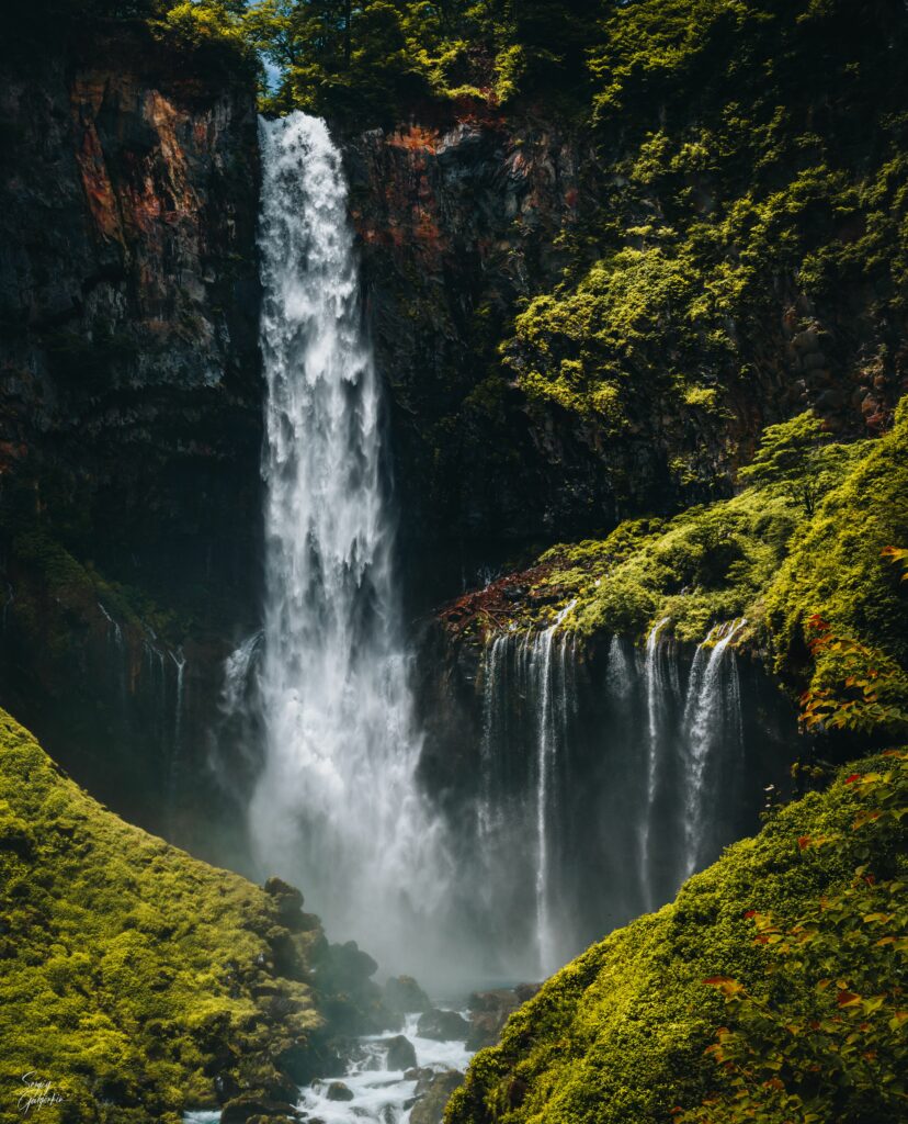 Breathtaking waterfall cascading down rugged cliff surrounded by lush moss and vibrant greenery Wallpaper