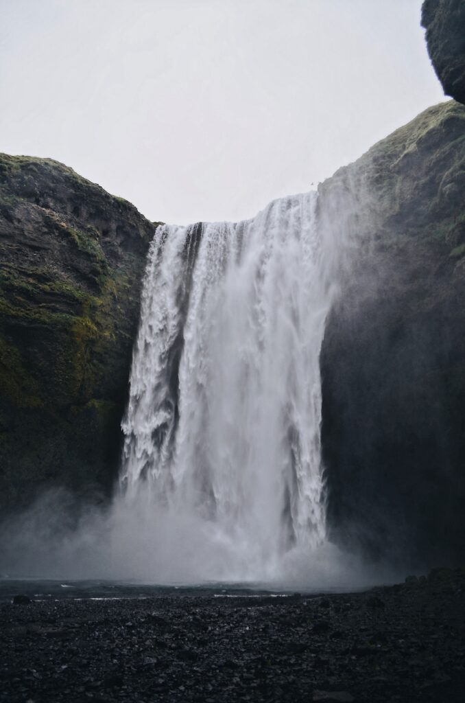 Majestic waterfall cascading over rugged cliff with mist and flowing river in natural tones Wallpaper