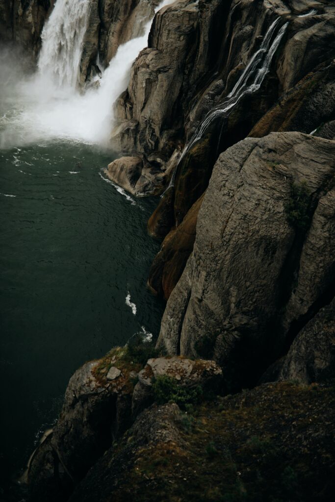 Powerful waterfall cascading rugged cliffs into deep green pool with textured rocks and lighting Wallpaper