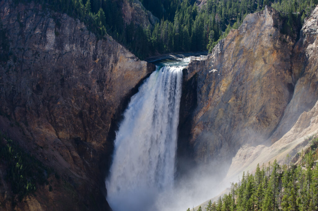 Majestic waterfall cascading over rugged cliffs surrounded by lush green forest in vibrant landscape Wallpaper
